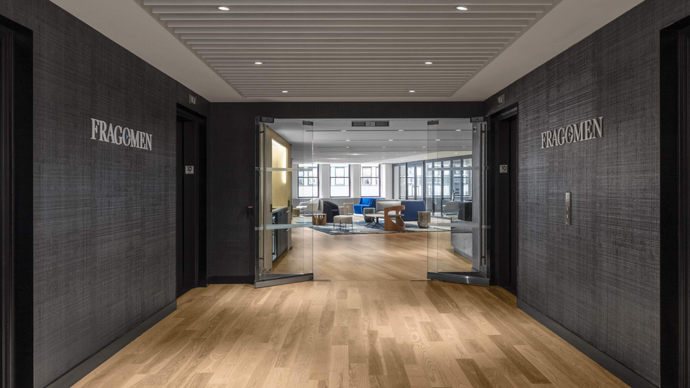 This New York building, the Fragomen, has dark hardwood flooring and dark grey walls. It is opening into a large, open sitting area.