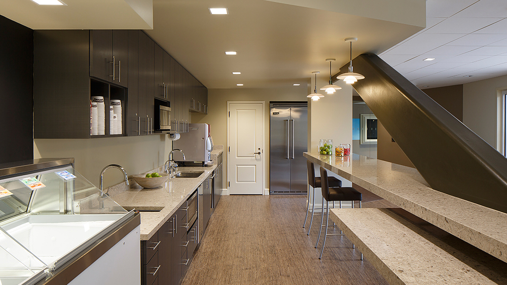 This kitchen space has an ice cream cooler, Nydree flooring and brown cabinets. There are granite countertops and silver appliances.