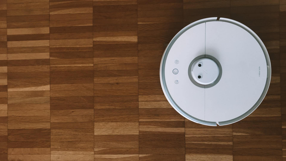 White robot vacuum cleaner on brown hardwood floor, gliding throughout the room.